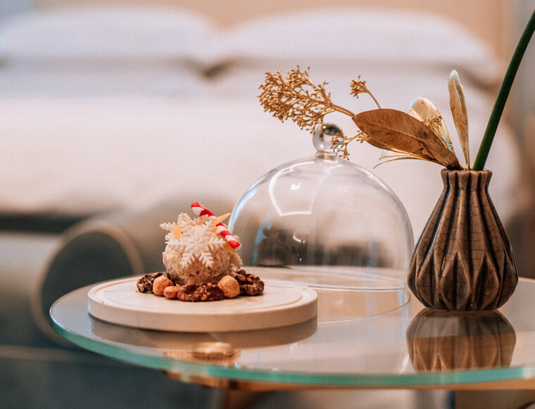 complimentary Christmas-themed pudding on a plate in a hotel room, with the soft focus of a luxurious bed in the background, adding a warm, festive touch.